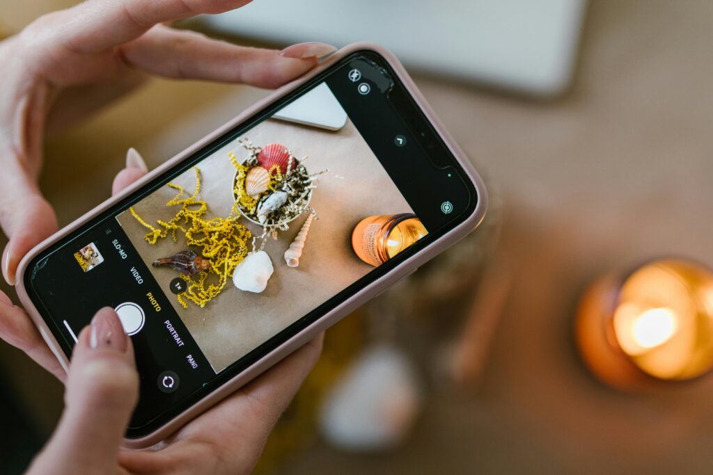 pexels photo 7310140 7310140 Close-up of hands using smartphone to photograph seashells and candles.
