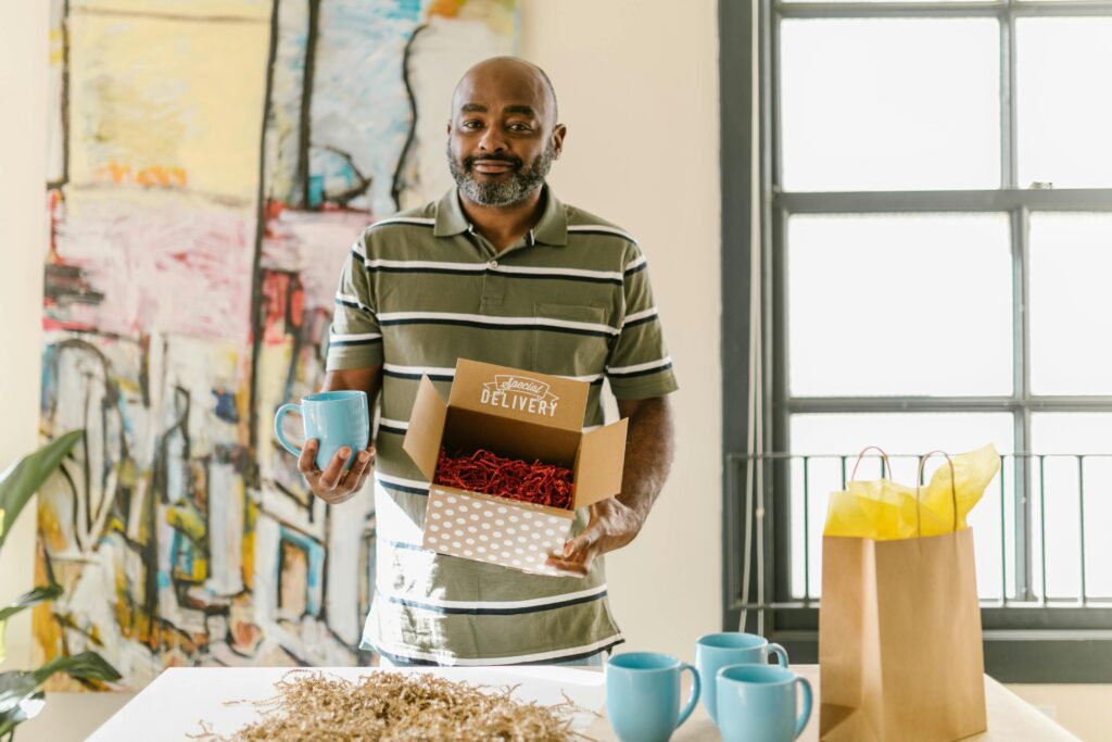 pexels photo 7310197 7310197 Man packing blue coffee mugs for delivery in a bright, artistic workspace.