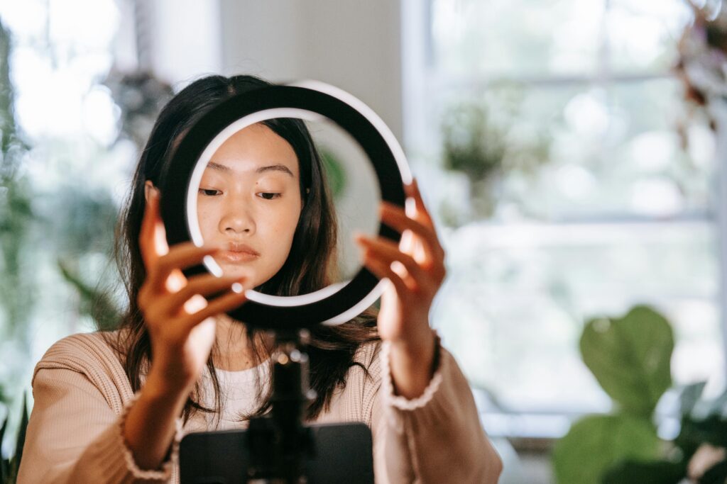 pexels photo 9414287 9414287 An Asian woman setting up a ring light indoors, focusing on her face and hands.
